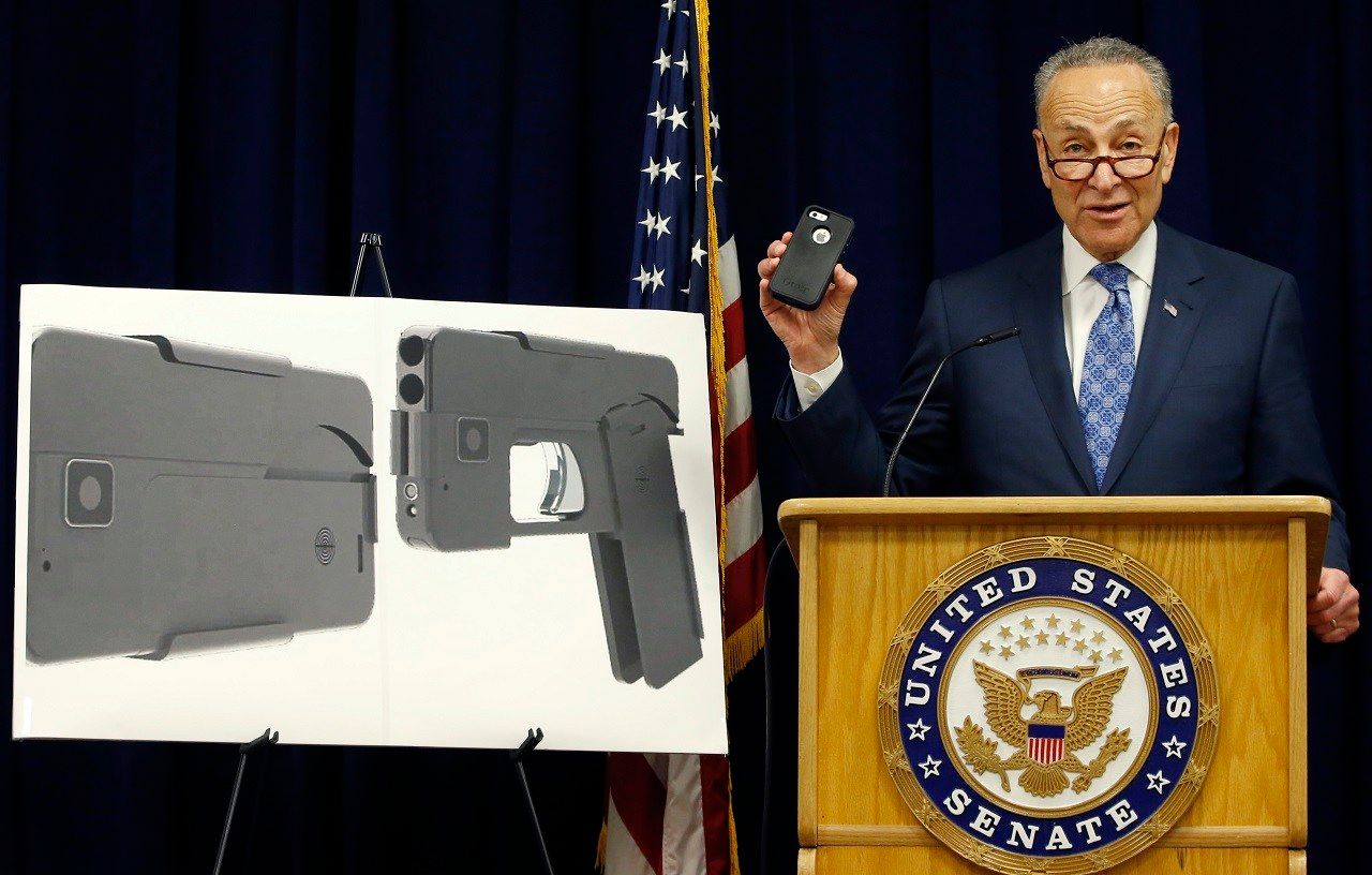 Standing beside photographs of a new product, U.S. Sen Charles Schumer, (D-New York), shown holding an iPhone 5S, voices his opposition to a handgun that appears to be a cell phone during a news conference in his office, Monday, April 4, 2016, in New York